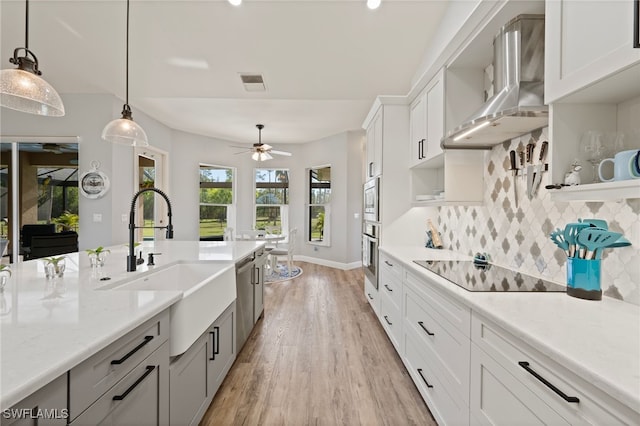 kitchen featuring decorative backsplash, wall chimney exhaust hood, appliances with stainless steel finishes, hanging light fixtures, and a sink