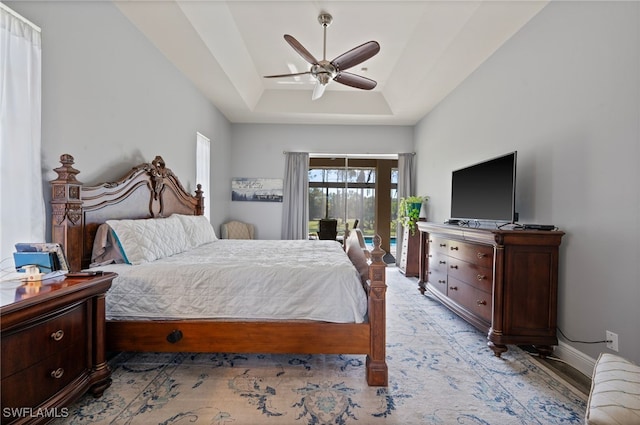 bedroom with ceiling fan, access to outside, a tray ceiling, and baseboards