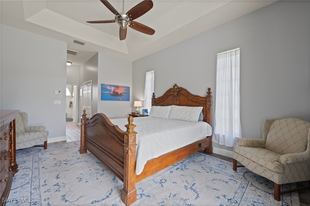 bedroom with a raised ceiling, visible vents, and baseboards