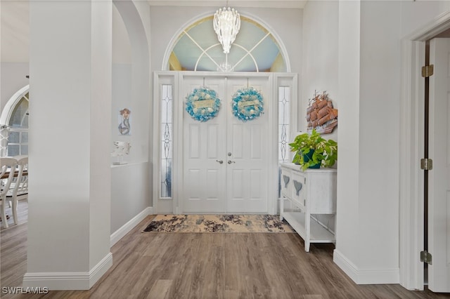 foyer featuring a notable chandelier, baseboards, arched walkways, and wood finished floors