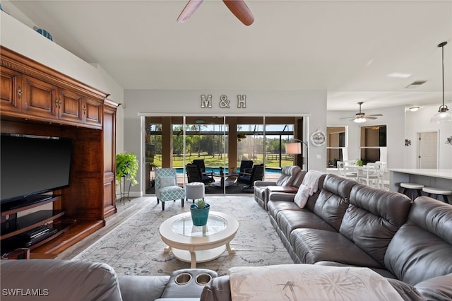 living room with a ceiling fan, visible vents, vaulted ceiling, and light wood finished floors