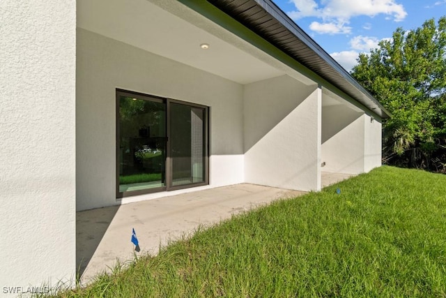 view of exterior entry featuring a patio area, a lawn, and stucco siding