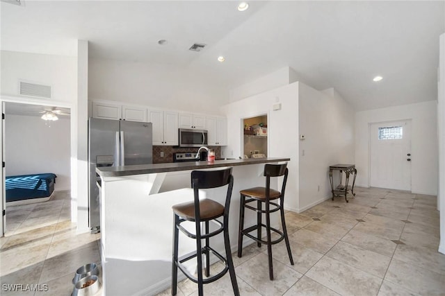 kitchen featuring stainless steel appliances, visible vents, white cabinetry, backsplash, and dark countertops