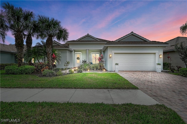 ranch-style home with a garage, a tile roof, decorative driveway, stucco siding, and a front lawn