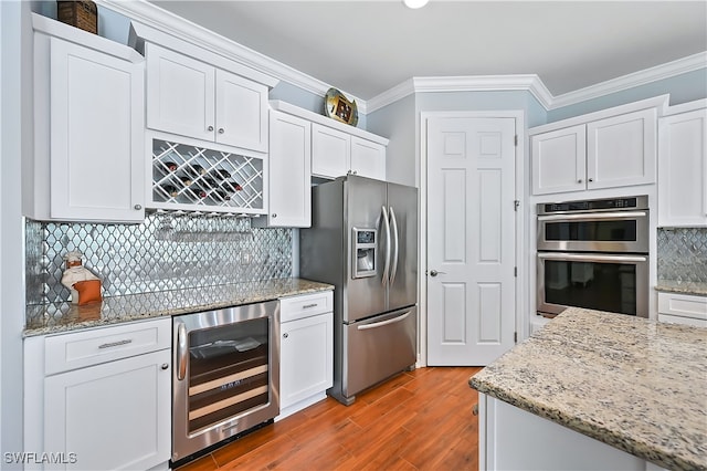 kitchen with light stone counters, wine cooler, appliances with stainless steel finishes, ornamental molding, and white cabinetry