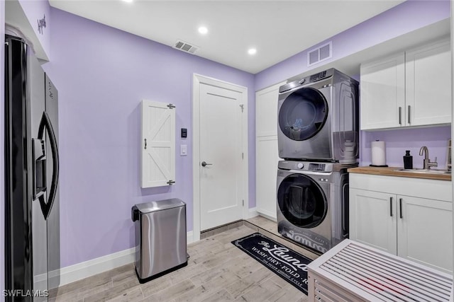 clothes washing area featuring a sink, cabinet space, visible vents, and stacked washer / dryer