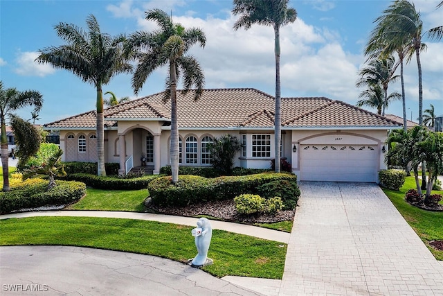 mediterranean / spanish home featuring a front lawn, decorative driveway, an attached garage, and stucco siding