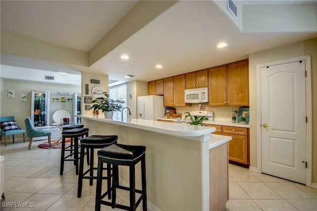 kitchen with white appliances, a kitchen breakfast bar, light tile patterned flooring, light countertops, and recessed lighting