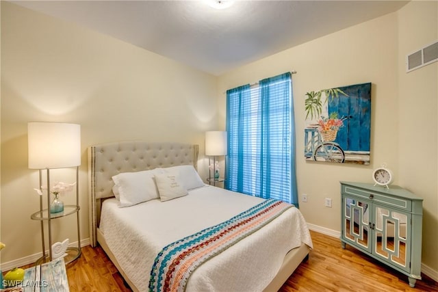 bedroom with baseboards, visible vents, and wood finished floors