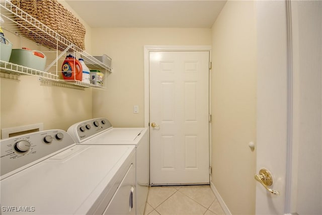 clothes washing area featuring laundry area, washing machine and dryer, baseboards, and light tile patterned flooring