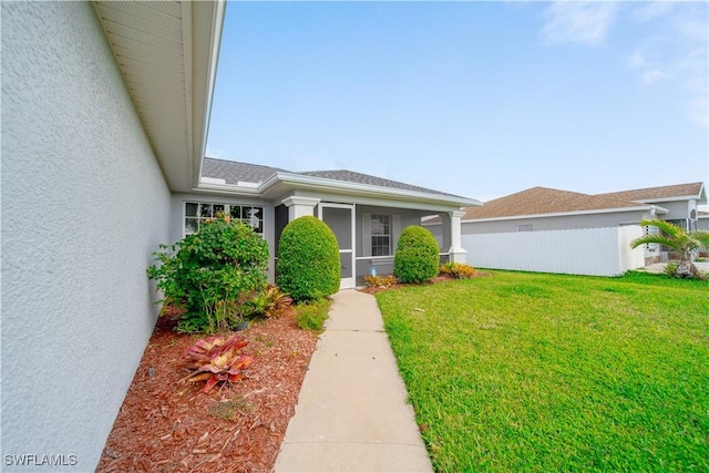 entrance to property with a lawn, fence, and stucco siding