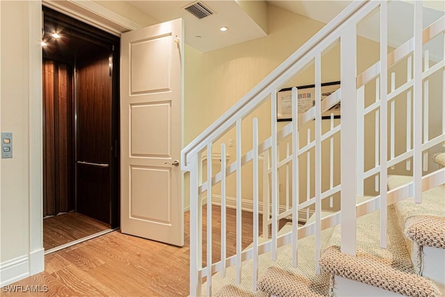 stairway featuring elevator, wood finished floors, visible vents, and recessed lighting