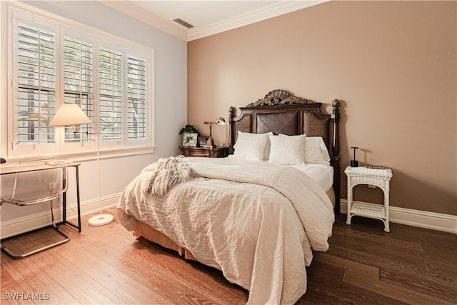 bedroom featuring ornamental molding, visible vents, baseboards, and wood finished floors