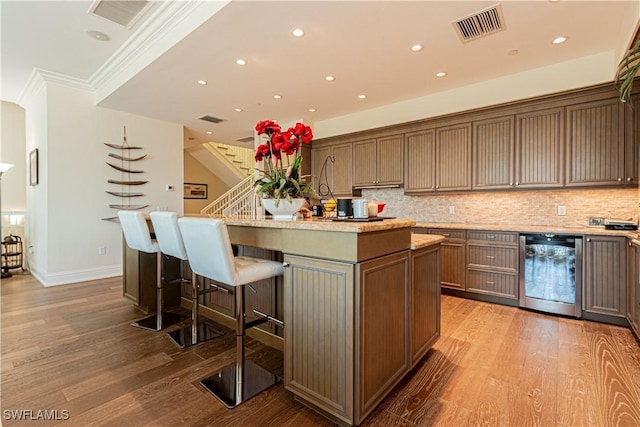 kitchen featuring tasteful backsplash, a center island with sink, visible vents, and wood finished floors