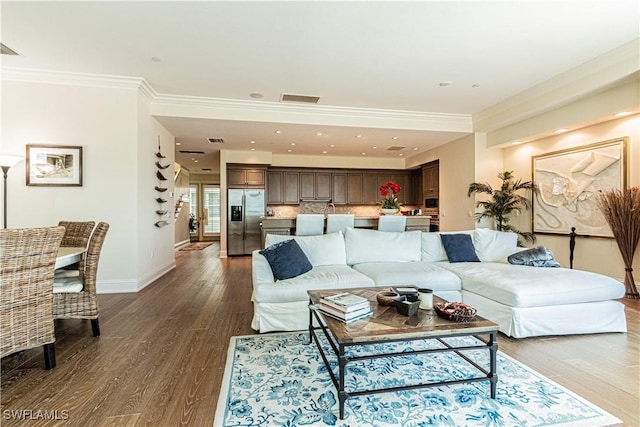 living room with dark wood-style flooring, visible vents, crown molding, and baseboards