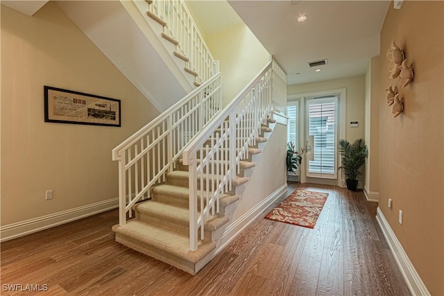 entryway with hardwood / wood-style floors, stairway, visible vents, and baseboards