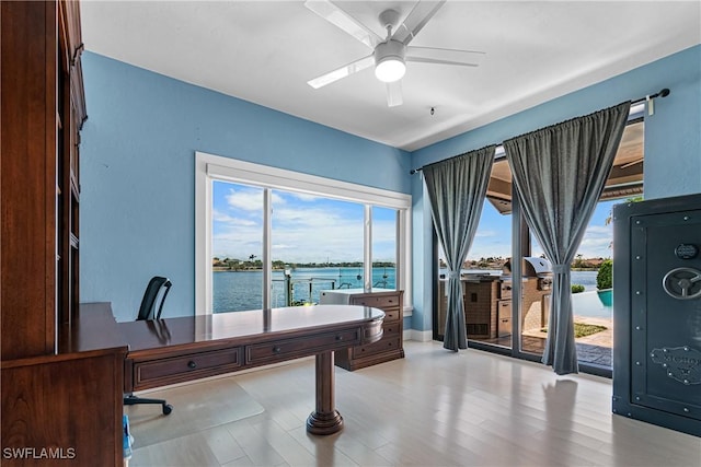 office area with a ceiling fan, a water view, and light wood-style flooring