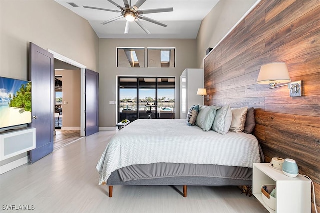 bedroom with wooden walls, visible vents, access to outside, a high ceiling, and light wood-type flooring