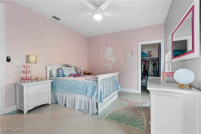 bedroom with a ceiling fan, visible vents, baseboards, light wood finished floors, and a walk in closet