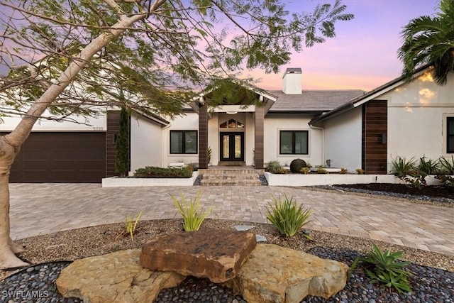 view of front of property featuring a garage, a chimney, french doors, and stucco siding