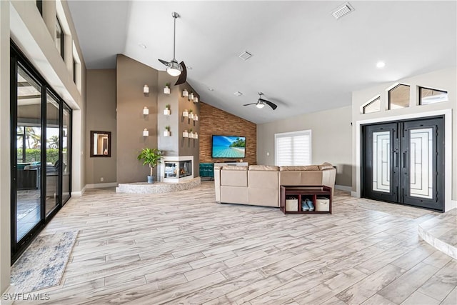 unfurnished living room with high vaulted ceiling, light wood-style flooring, a large fireplace, visible vents, and french doors