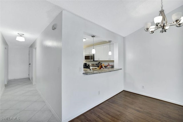 interior space featuring a notable chandelier, white cabinetry, stainless steel appliances, baseboards, and hanging light fixtures