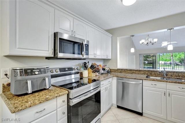 kitchen with light stone countertops, light tile patterned floors, white cabinets, stainless steel appliances, and a sink