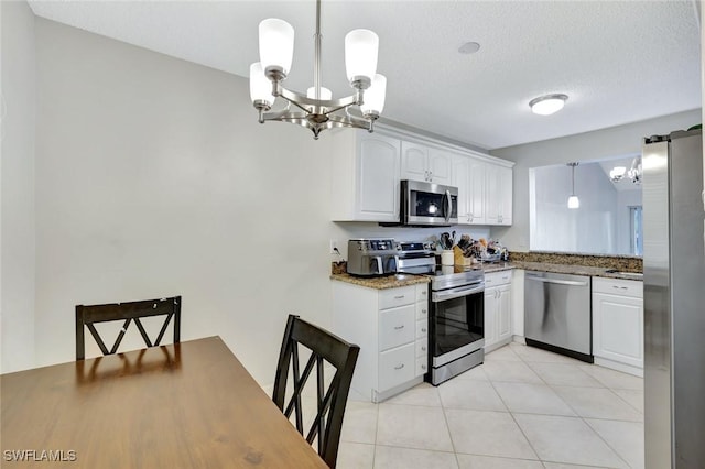 kitchen featuring dark stone countertops, an inviting chandelier, light tile patterned flooring, white cabinets, and stainless steel appliances