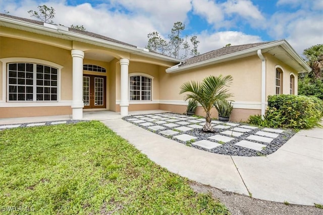 property entrance with french doors, a lawn, and stucco siding