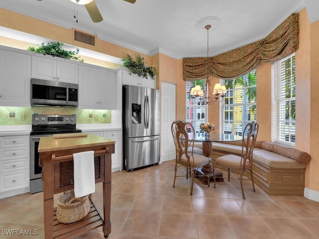 kitchen with light tile patterned floors, stainless steel appliances, white cabinets, ornamental molding, and backsplash