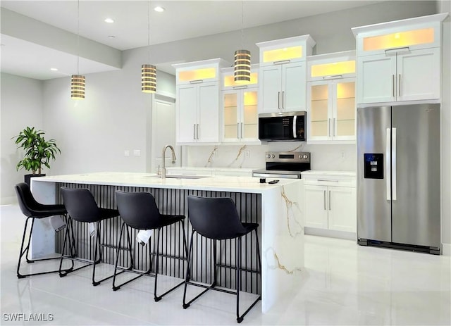 kitchen featuring a kitchen island with sink, a breakfast bar, a sink, appliances with stainless steel finishes, and tasteful backsplash