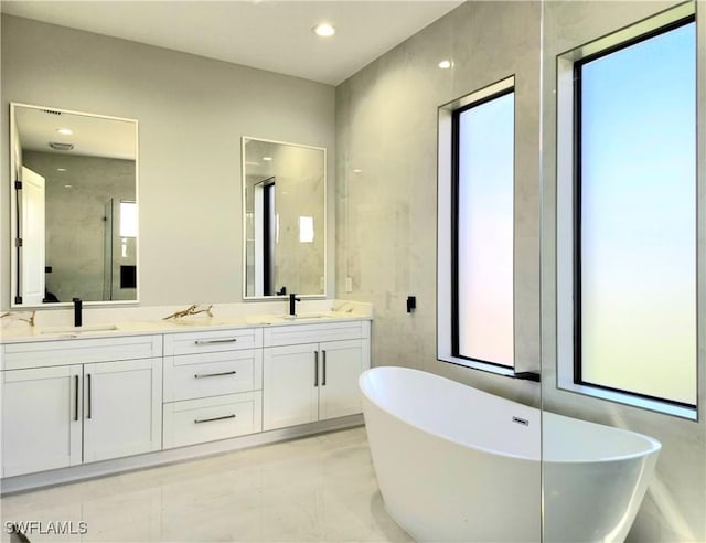 full bathroom featuring double vanity, a freestanding tub, a sink, and recessed lighting