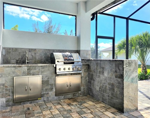 view of patio featuring glass enclosure, a sink, and area for grilling