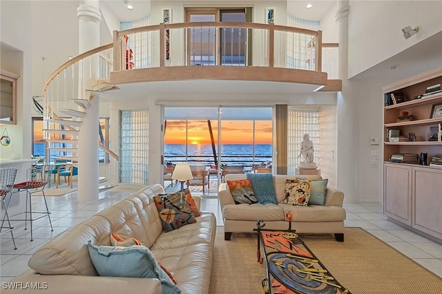 living area featuring stairs, light tile patterned floors, a water view, and a towering ceiling