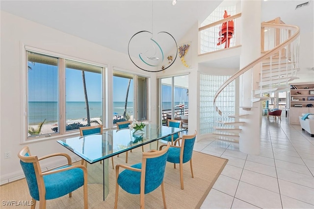 dining space with visible vents, a water view, stairs, light tile patterned floors, and a towering ceiling