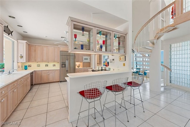 kitchen featuring a sink, a kitchen breakfast bar, a peninsula, light tile patterned flooring, and built in appliances