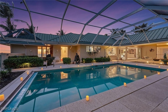 pool at dusk featuring an outdoor pool, a patio, and a lanai