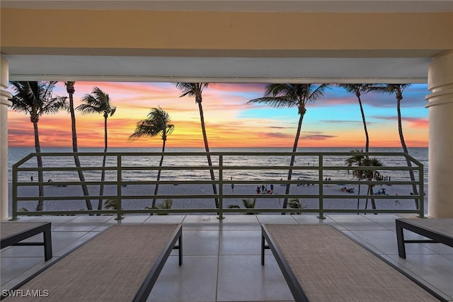 patio terrace at dusk featuring a beach view, a balcony, and a water view