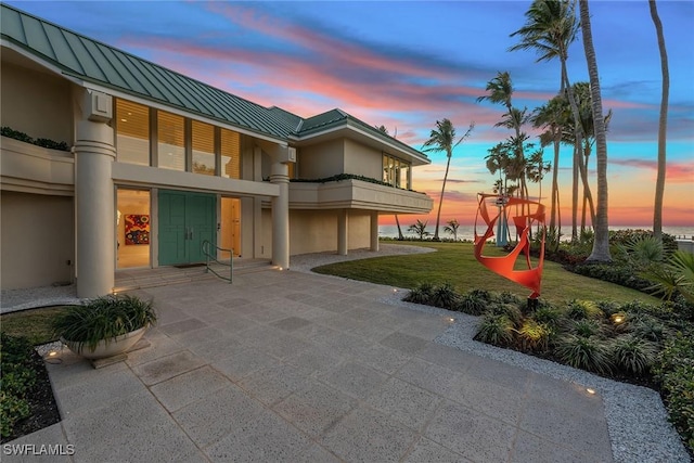 30 3rd Ave S, Naples, FL 34102 - back of property at dusk with a standing seam roof, a balcony, stucco siding, metal roof, and a yard