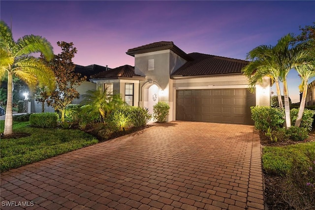 mediterranean / spanish home with an attached garage, decorative driveway, and stucco siding