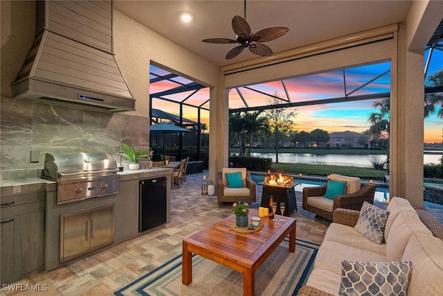 patio terrace at dusk with an outdoor living space with a fire pit, a water view, grilling area, exterior kitchen, and a lanai