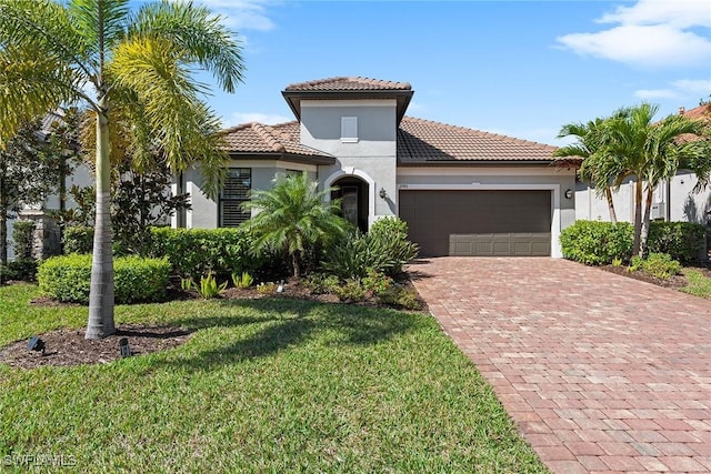 mediterranean / spanish home featuring stucco siding, a tiled roof, an attached garage, decorative driveway, and a front yard