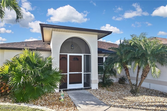 entrance to property featuring a shingled roof and stucco siding