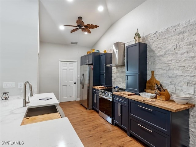 kitchen featuring butcher block counters, a sink, appliances with stainless steel finishes, light wood-type flooring, and wall chimney exhaust hood