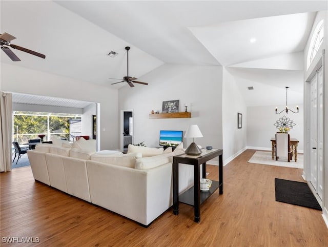 living area featuring light wood-style floors, visible vents, vaulted ceiling, and ceiling fan with notable chandelier