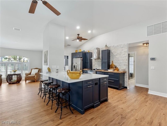 kitchen featuring stainless steel fridge, visible vents, light wood-style floors, wall chimney range hood, and a kitchen bar