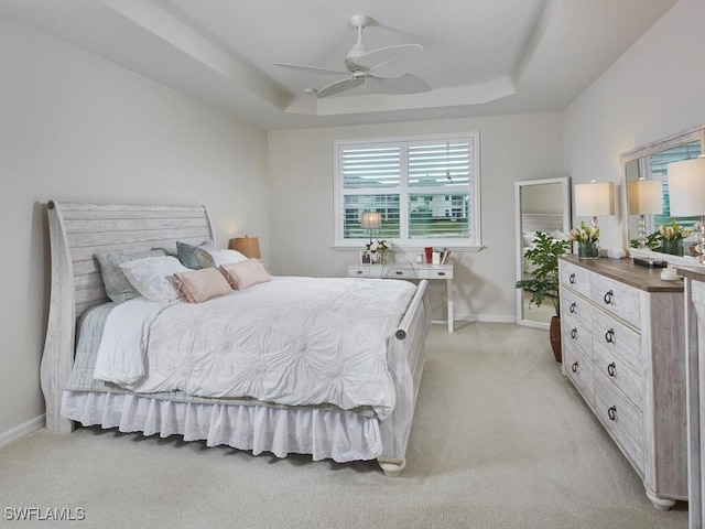 bedroom featuring baseboards, a raised ceiling, light carpet, and ceiling fan