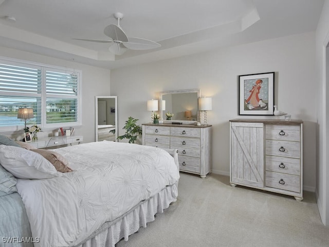 bedroom with a tray ceiling, light colored carpet, baseboards, and ceiling fan