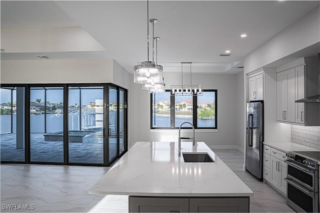 kitchen with stainless steel appliances, a sink, light stone countertops, tasteful backsplash, and an island with sink