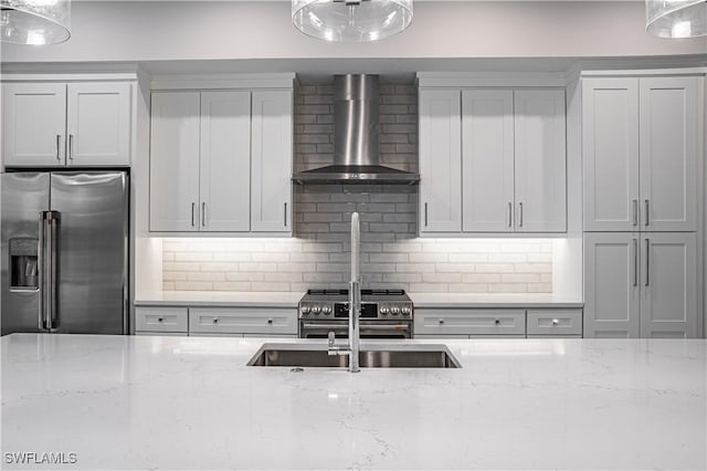 kitchen featuring premium appliances, light stone counters, wall chimney range hood, and decorative backsplash